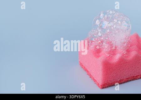 Rosafarbener Schwamm mit Seifenschaum auf blauem Hintergrund Stockfoto