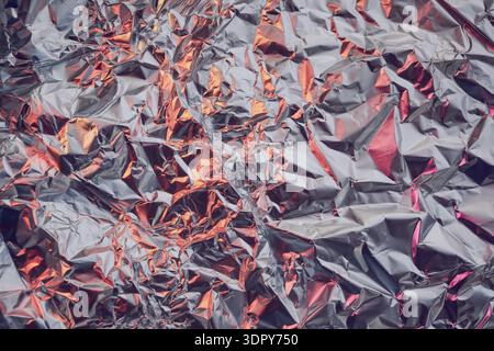 Zerknitterte Oberfläche aus Aluminiumfolie für eine abstrakte metallische Textur mit warmen Lichtreflexionen Stockfoto