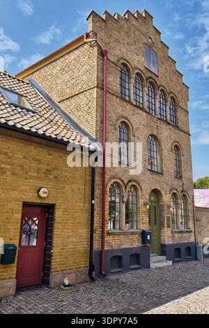 Landskrona, Schweden - 08. August 2025: Blick auf ein markantes gelbes Backsteingebäude mit Bogenfenstern und einer roten Tür im Kontrast zum blauen Himmel. Stockfoto