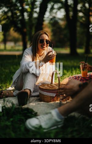 Frau genießt ein sonniges Picknick in einem Park mit Orangensaft und Freunden Stockfoto