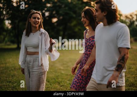 Drei Freunde laufen in einem sonnigen Park, lächeln und unterhalten sich, während sie draußen spazieren Stockfoto