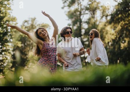 Drei Freunde tanzen in einem sonnigen Park, genießen gemeinsam Musik und Lachen Stockfoto