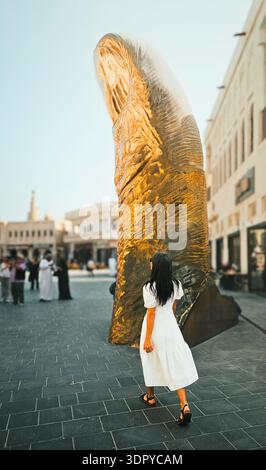 Doha, Katar - 22. januar 2026: Frau geht in Richtung monumentaler Daumenskulptur im Katara Cultural Village Doha mit zeitgenössischer öffentlicher Kunst u Stockfoto