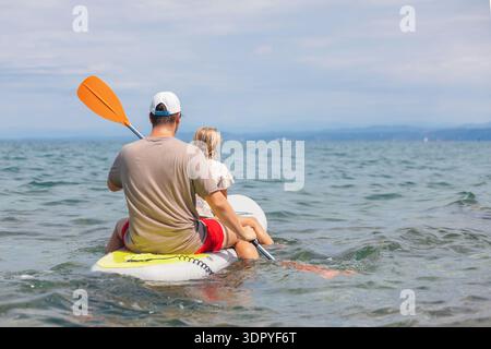 Ein Bruder und eine Schwester genießen an einem sonnigen Sommertag Stand Up Paddleboarden auf dem Meer, während sie gemeinsam Spaß haben. Stockfoto