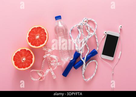 Gesunde Lebensstil-Gegenstände auf rosa Hintergrund mit Früchten, Wasser und Fitness-Ausrüstung Stockfoto