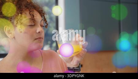 Lockige Frau riecht ein Glas Orangensaft in der Küche am Fenster, rosa Spitze, Bokeh Stockfoto