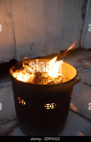 Brennendes Feuer im Metalleimer mit glühender Glut, rustikale Außenumgebung, warmes Umgebungslicht, Nachtszene Stockfoto