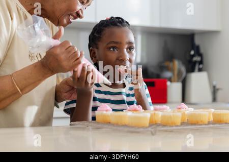 Seniorin und Jugendmädchen dekorieren Vanillemuscheln mit Backteigbeutel in der Küche Stockfoto