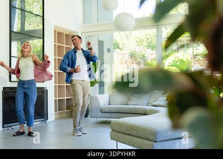 Verschiedene Paare tanzen zusammen in einem hellen, modernen Wohnzimmer in der Nähe eines grauen Sofas und Glastüren Stockfoto