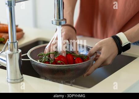 Hände, die rote Rebsorte in einem Sieb aus Stahlgewebe unter einem laufenden Chromhahn spülen, Karotten in der Nähe Stockfoto
