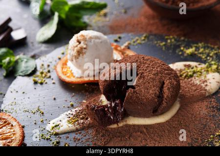 Schokoladendessert mit Melting Center, serviert auf einem schwarzen Teller mit Eis und Orange Stockfoto