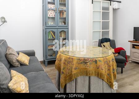 Wohnzimmereinrichtung mit komfortablem Sofa, rundem Tisch mit gemusterter Tischdecke und klassischem blauem Schrank Stockfoto