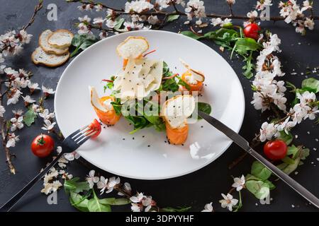 Salat mit Lachs und Käse auf einem weißen Teller mit Blumen und Tomaten Stockfoto