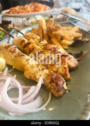 Traditionelle griechische Chicken Souvlaki Spieße mit knusprigen Pommes Frites, Zwiebeln und Zitronen auf einem Teller. Stockfoto