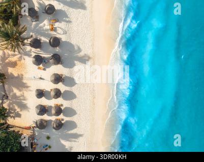 Aus der Vogelperspektive auf Palmen, Sonnenschirme am Sandstrand, blaues Meer Stockfoto