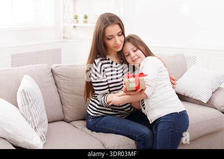 Mutter und Tochter teilen sich einen Moment, während sie in einem gemütlichen Wohnzimmer ein Geschenk erhalten Stockfoto
