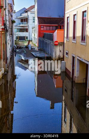 Enge überflutete Straße zwischen farbenfrohen Gebäuden mit orangefarbenen, gelben und weißen Fassaden, die sich in ruhigem Wasser spiegeln, mit einem roten Verkehrsschild und Res Stockfoto