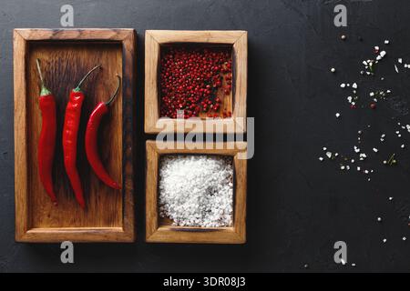 Rote Chili-Paprika und Gewürze in Holzkisten auf dunkler Oberfläche für Kochaktivitäten Stockfoto