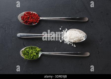 Verschiedene Gewürzarten in Metalllöffeln auf dunkler Oberfläche Stockfoto