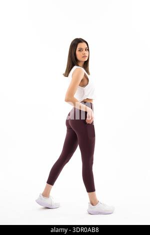 Eine Frau in einem weißen Tanktop und einer schwarzen Hose läuft auf weißem Hintergrund. Konzept von Fitness und Gesundheit, da die Frau in Workout-Kleidung gekleidet ist Stockfoto