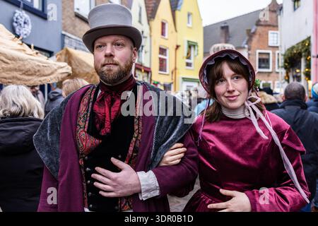 Deventer, Overijssel, Niederlande - 14.12.2025: Zwei Personen in viktorianischen Kostümen spazieren durch eine geschmückte Straße während einer feierlichen öffentlichen Veranstaltung. Stockfoto