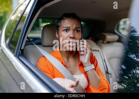 Schwarze Frau, die auf dem Rücksitz sitzt und mit besorgtem Ausdruck auf dem Handy spricht Stockfoto