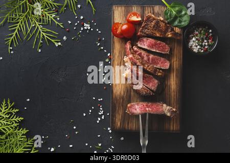 Gegrilltes Steak auf einem Holzbrett mit Tomaten und Kräutern an einem Esstisch Stockfoto
