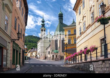Majestätische weiße Burgtürme krönten den grünen Hügel mit Blick auf das Meer aus roten Dächern, eingebettet zwischen bewaldeten Hängen unter blauem Himmel. Banská Štiavnica Dist Stockfoto