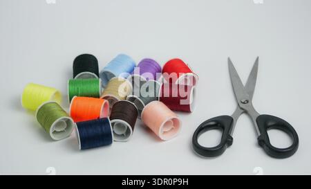 Bunte Nähgarnspulen mit Schere auf weißem Hintergrund. Schneiderei, Heimwerkerarbeit und handgefertigtes Konzept. Studio-Aufnahme mit Kopierraum, hoher Auflösung Stockfoto