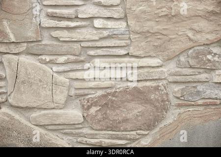 Beige Steinmauer mit unregelmäßigen Platten und rauer Textur in neutralen Tönen. Horizontale Nahansicht mit Kopierraum. Stockfoto