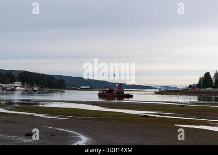 Port Hardy, BC, Kanada - 25. Juni 2024: Arbeitskahn nahe der Quarterdeck Marina bei Ebbe mit Gezeitenschlamm und immergrüner Küste. Stockfoto