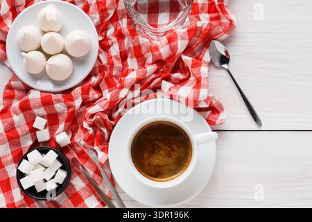 Kaffee mit Meringue und Zucker auf einer rot karierten Tischdecke in einer einfachen Umgebung Stockfoto