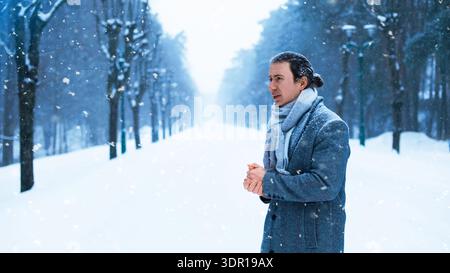 Ein deprimierter Mann zittert und reibt sich die Hände in einem eiskalten Winterpark. Er steht allein in einer verschneiten Gasse, mit dem sich verschlechternden Wetter, starkem Schneesturm, an Stockfoto