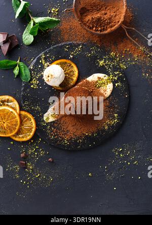 Dessert mit Schokolade, Eis, Obst und Gewürzen auf einem schwarzen Teller in einer Küche Stockfoto