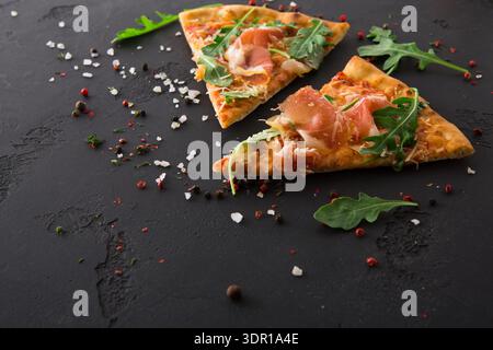 Köstliche Pizzastücke mit Prosciutto und Arugula auf dunklem Hintergrund Stockfoto