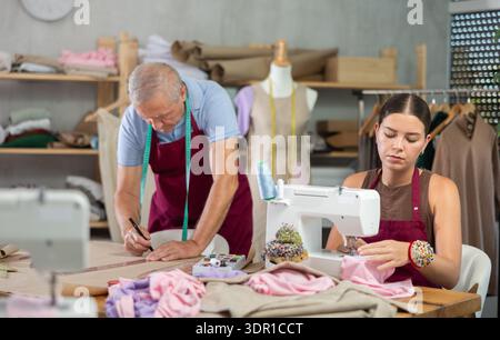 Junge Frau, die männliche Assistentin mit Zeichenmuster auf Papier näht Stockfoto