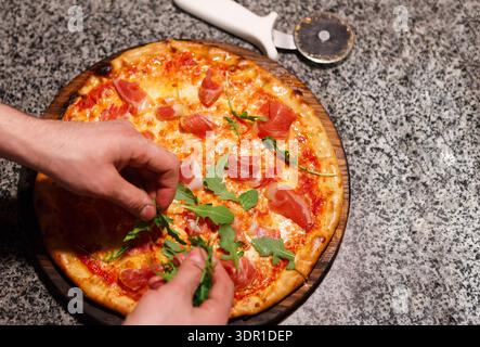 Am Abend eine frische Pizza mit Belägen an einem Küchentisch zubereiten Stockfoto