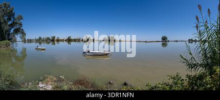 Panoramablick auf kleine Boote, die auf ruhigem Wasser an der Isla minima in den Marschen von Guadalquivir in Andalusien, Spanien schwimmen. Stockfoto