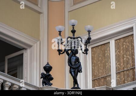 Cadiz, Spanien - 26. September 23: Dekorative Cherub-Statue mit einer mehrarmigen Lampe auf einem Balkon im historischen Innenhof des Atriums in Cádiz, Andalus Stockfoto
