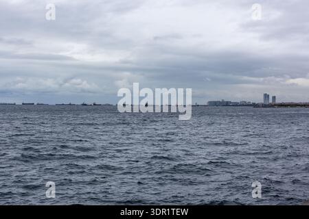 Frachtschiffe auf See. Abgehacktes Wasser unter einem grauen bedeckten Himmel. Entfernte Skyline von Istanbul und Uferpromenade am Horizont. Stockfoto