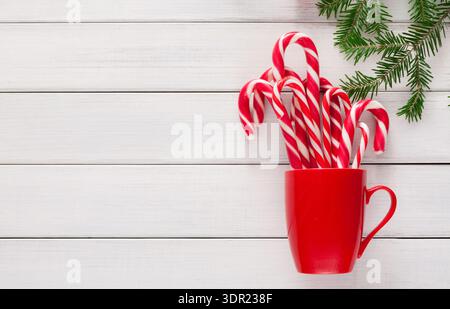 Festliche Sammlung von Zuckerstangen in rotem Becher mit grünem Kiefernzweig auf Holzoberfläche Stockfoto