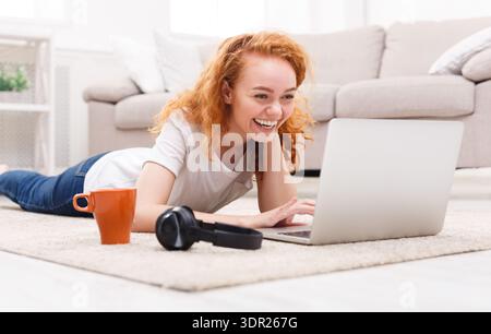Junge Frau genießt Zeit Online, während sie auf dem Boden in einem hellen Wohnzimmer liegt Stockfoto