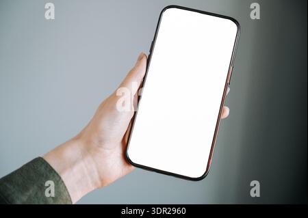 Nahaufnahme einer Hand, die ein modernes Smartphone mit einem leeren weißen Bildschirm hält. Dank minimalem Hintergrund und Kopierraum ist dieses Bild ideal für das Presen von Apps Stockfoto