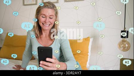 Lächelnde reife Frau mit hellblauem Oberteil, die ein schwarzes Smartphone auf dem Bett im Schlafzimmer hält, AI-Überzug Stockfoto