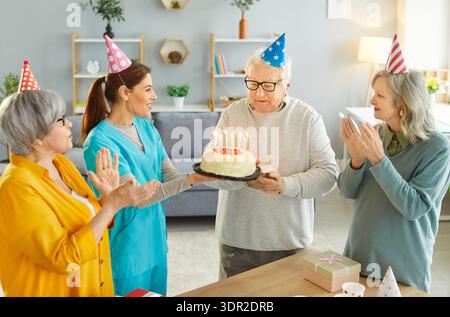 Schwester bringt Kuchen für Seniorenmann, der mit alten Freunden im Pflegeheim Geburtstag feiert. Stockfoto
