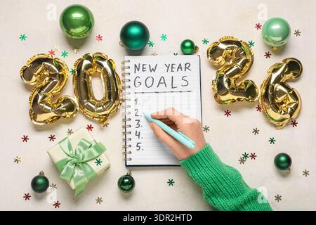 Frau mit Figur 2026, Geschenkbox und Weihnachtsdekor, die To-do-Liste auf weißem Hintergrund schreibt Stockfoto