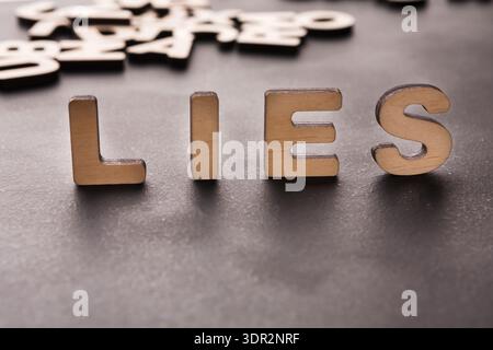 Die Schreibweise von Holzbuchstaben liegt auf einer dunklen Oberfläche, während andere Buchstaben im Hintergrund angezeigt werden Stockfoto