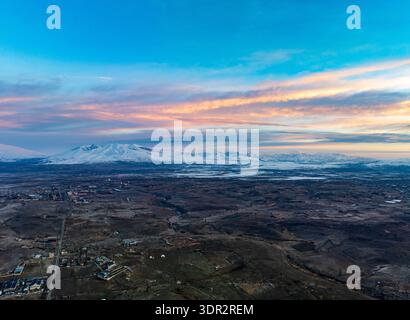Panoramablick auf die Berglandschaft von Aragats bei Sonnenuntergang mit einer kleinen Stadt im Tal Stockfoto