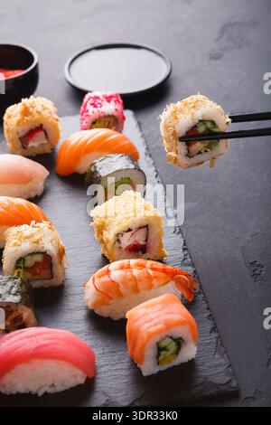Sushi-Kollektion auf schwarzem Schiefer mit leuchtenden Farben und verschiedenen Rollentypen Stockfoto