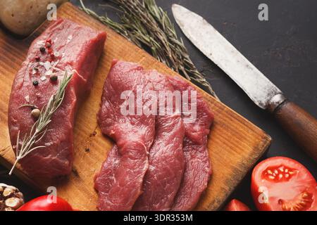 Auswahl an rohem Rindfleisch und frischen Zutaten auf einem Holzbrett in einer Küche Stockfoto